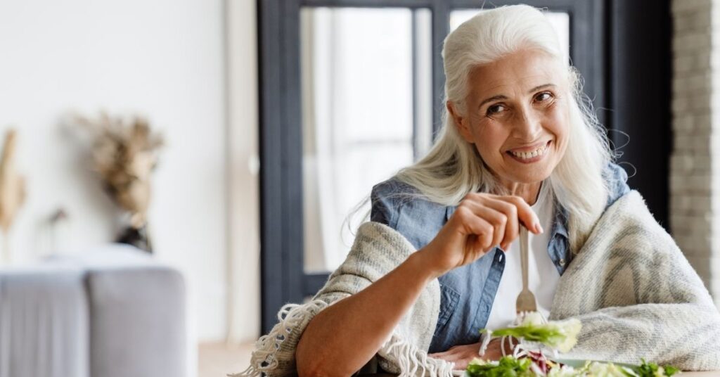 Ältere Frau isst eine gesunde Mahlzeit– eine purinarme Ernährung kann helfen, den Harnsäurespiegel zu senken und Gichtanfälle zu vermeiden.