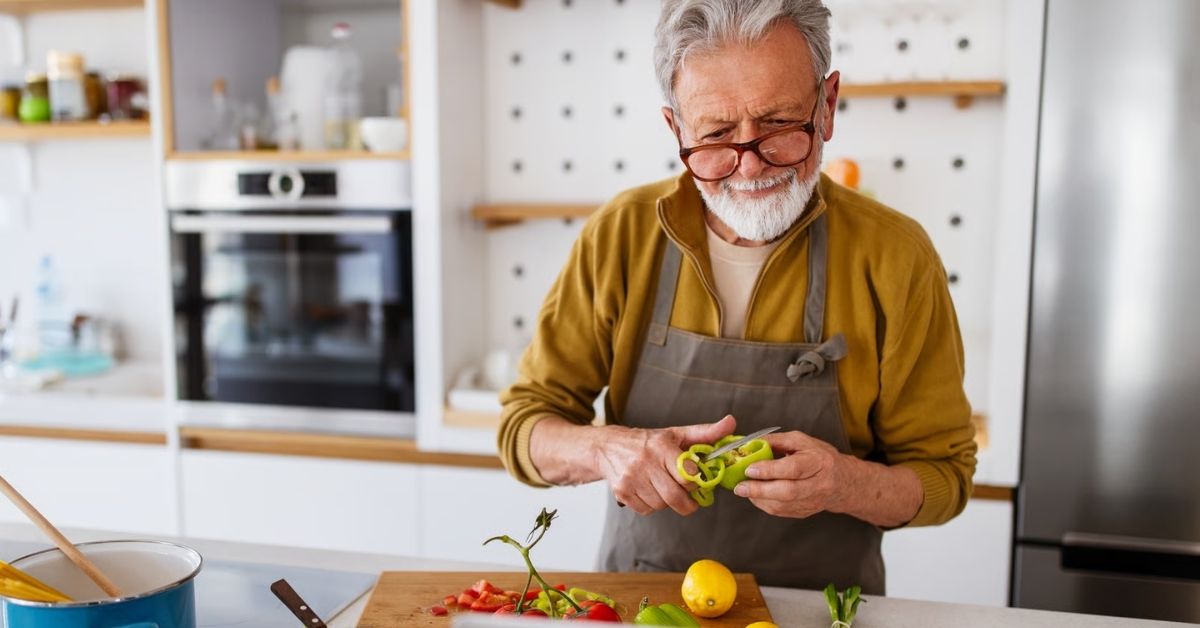 Älterer Mann schneidet in der Küche frisches Gemüse für eine purinbewusste Ernährung