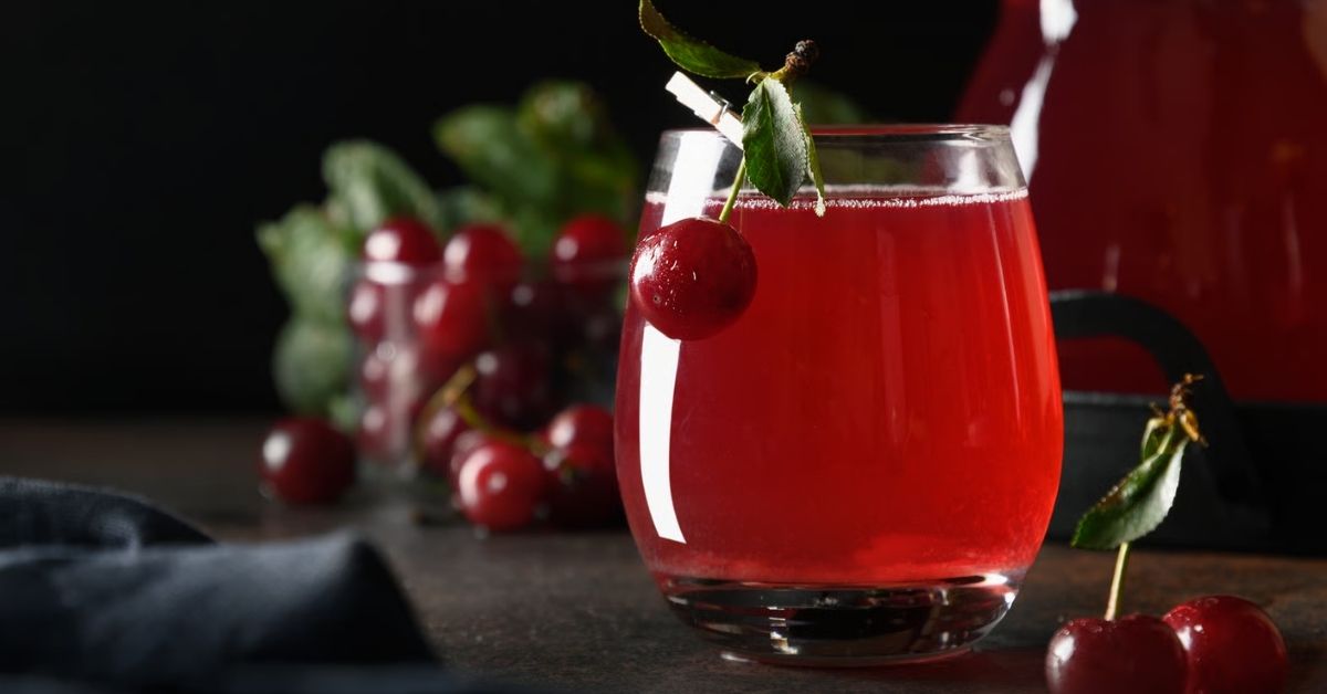 Glas mit rotem Sauerkirschsaft und frischen Kirschen auf dunklem Untergrund